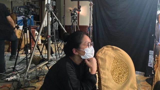 Moon Tsui menonton syuting film dengan kamera dan lampu di latar belakang