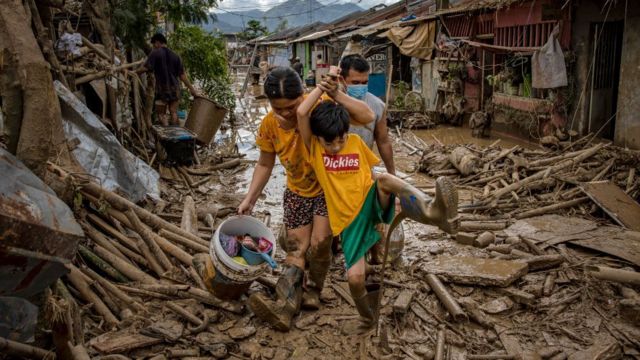 Seorang anak membersihkan lumpur dari sepatu botnya saat warga mengarungi air banjir berlumpur dan puing-puing di sebuah desa setelah Topan Vamco menerjang Rodriguez, Provinsi Rizal, Filipina, 14 November 2020.